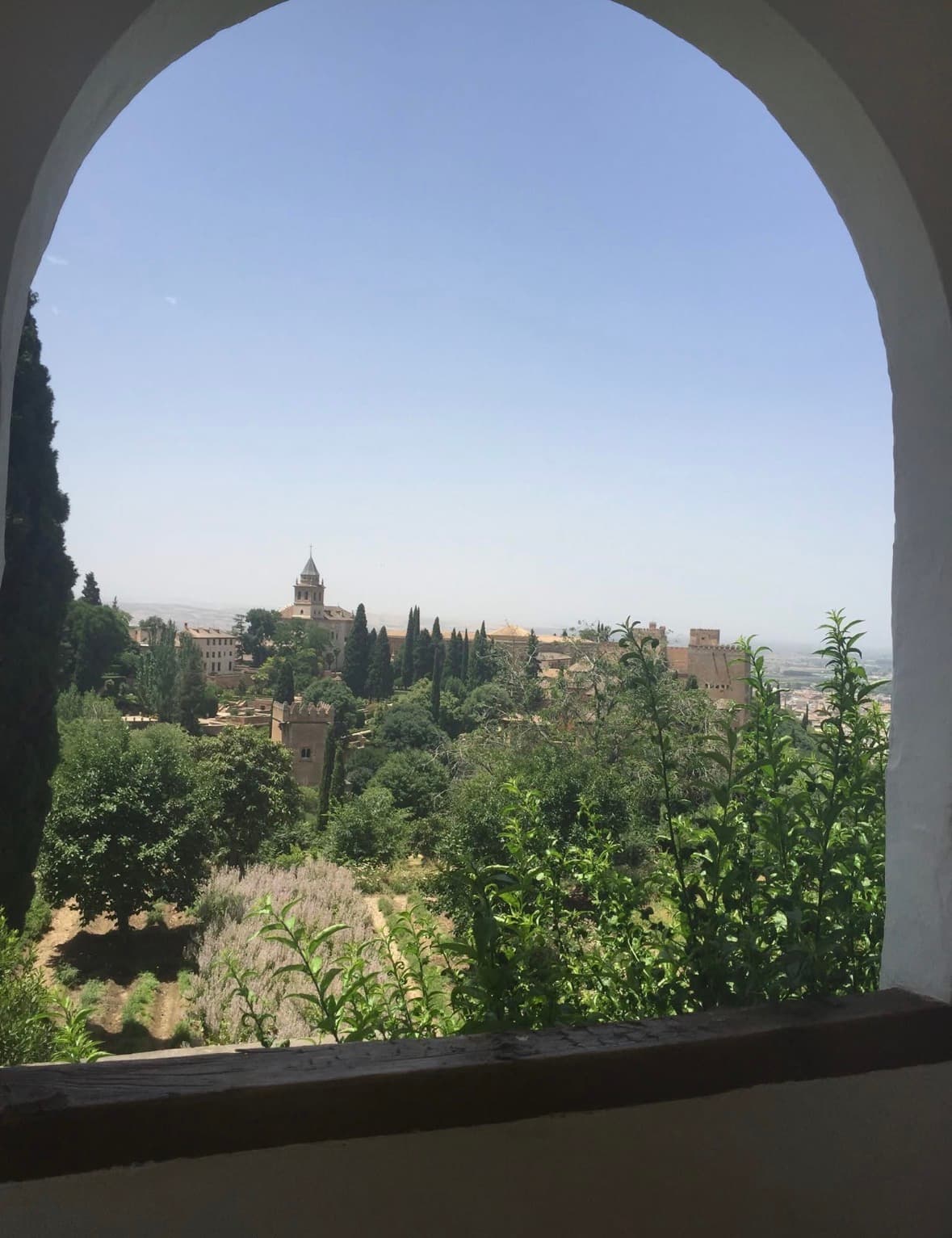 A hillside monastery and tower seen through a stone archway in Granada, Spain